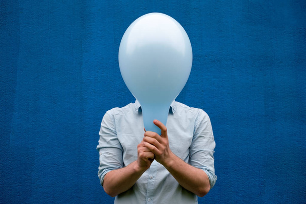 Beyaz bir adam yüzü mavi bir balon ile kapsar. - Fotoğraf, Görsel