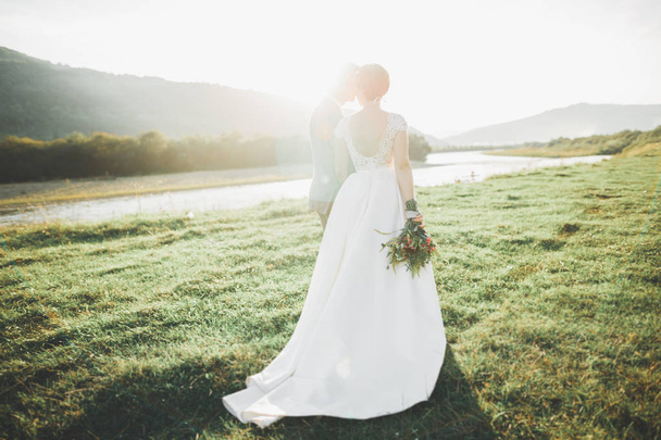 Young newly wed couple, bride and groom kissing, hugging on perfect view of mountains, blue sky - Foto, Bild