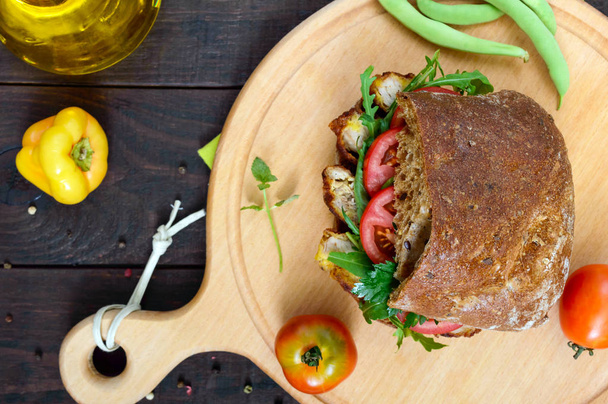 Большой сэндвич с кусочками мяса, рукколой, помидорами, хлопьями чиабатта на разделочной доске
  - Фото, изображение