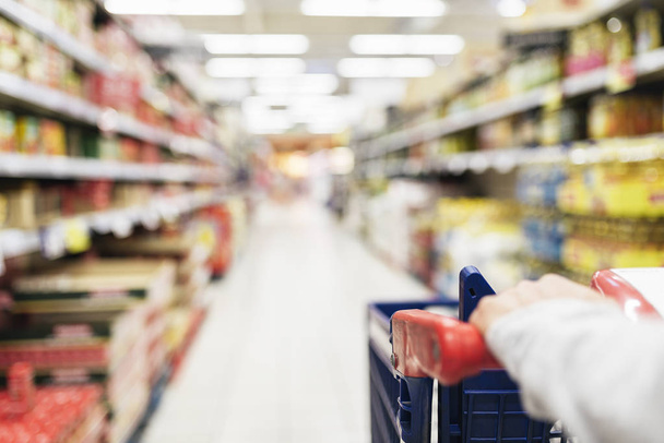 Close up of woman using shopping cart in supermarket. Background - Foto, Imagem