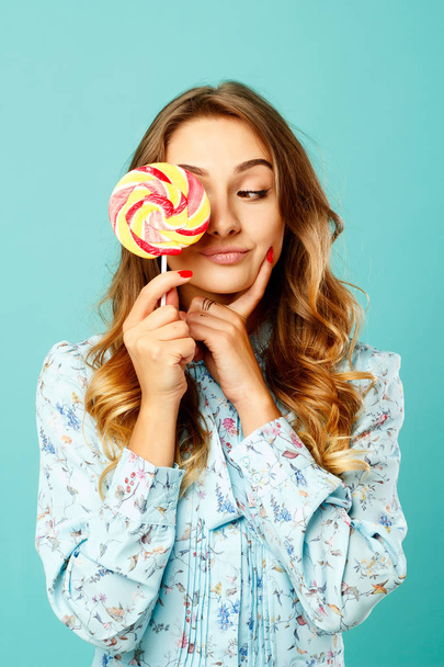 Young pretty smiley woman holding lollipop in hands over blue ba - Foto, Imagem