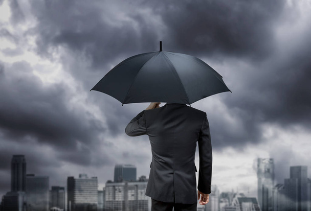 zakenman houden paraplu onder regen onweer met stad achtergrond - Foto, afbeelding