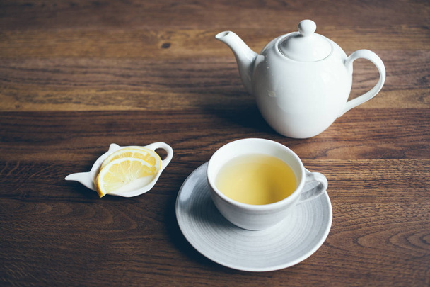 Крупный план чашки горячего чая с лимоном и чайником на коричневом деревянном столе
. - Фото, изображение