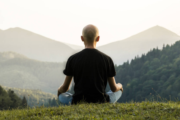 Skinny male person doing yoga sits in lotus position top of the hill in ukrainian carpathian mountains - Fotografie, Obrázek