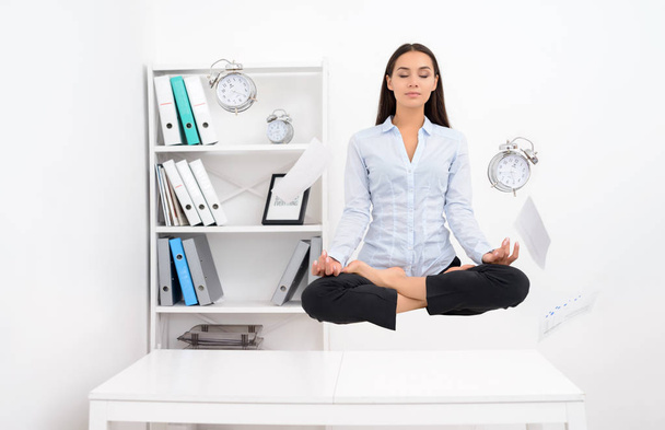 Женщина левитирует над офисным столом и медитирует в позе лотоса
 - Фото, изображение