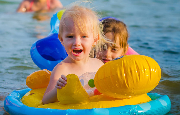 Niña de tres años nada en el mar sentada en el anillo de goma, nadando y sonriendo felizmente
. - Foto, Imagen