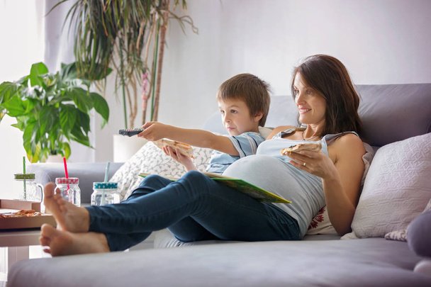 Young pregnant mother and her boy, eating tasty pizza at home, w - Foto, afbeelding