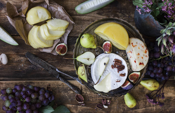 Different cheese, fresh fruits and garden flowers on old wooden background - Foto, Imagen