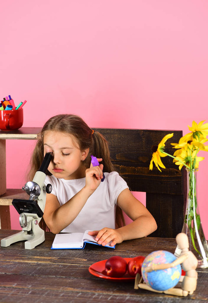 Girl with concentrated face looks into microscope - Zdjęcie, obraz