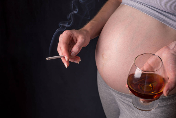 Una mujer embarazada con vientre sosteniendo un vaso de whisky y un cigarrillo. Concepto alcohol y malos hábitos durante el embarazo - Foto, Imagen