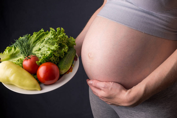 Terhes nő hasa egy tányér zöldséges tartja. Koncepció súlykontroll és az egészséges táplálkozás a terhesség alatt - Fotó, kép
