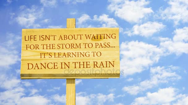 Life isn't about waiting for the storm to pass. It's learning to dance in the rain, Words on a wooden sign against time lapse clouds in the blue sky.  - Footage, Video