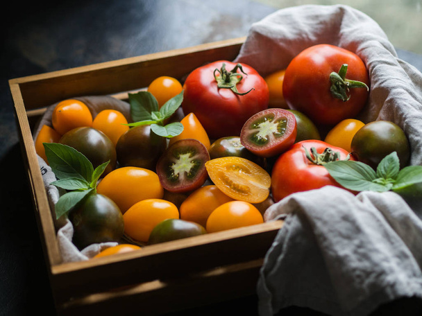 Colorful tomatoes  in wooden tray on dark background - Фото, зображення