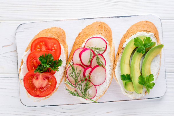 Mini sándwiches con queso crema, verduras y aguacate. Variedad de sándwiches sobre fondo blanco, vista superior
 - Foto, Imagen