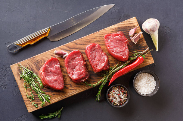 Filet mignon steaks and spices on wood at black background - Foto, Imagen