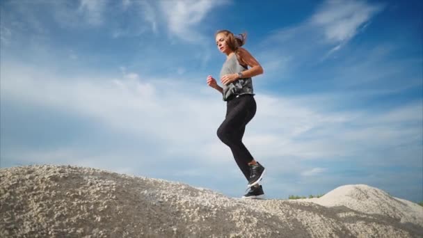 Μια νεαρή γυναίκα με ένα καλό σχήμα τρέχει κάτω από το υψηλό πέτρες σε ένα ψηλό βουνό - Πλάνα, βίντεο