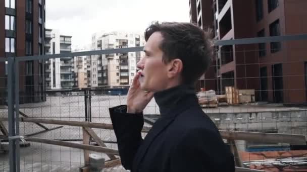Young man in suit using smartphone. House under construction at background - Video