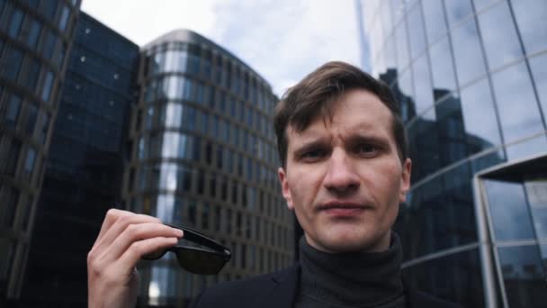 Young man in suit putting on sunglasses. Business centre building at background - Footage, Video