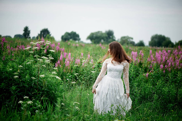 Beautiful bride in bright lace dress. In a field with Ivan-tea. Natural beauty, minimal makeup and loose hair.A child of nature - Фото, зображення