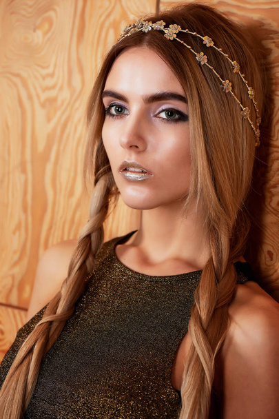 Beautiful girl model in the Studio shooting beauty. Gold makeup, long hair, golden top. Warm - Photo, image