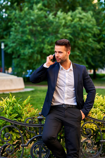Young man waiting in a park and talking on a phone - Фото, изображение
