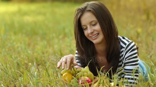 junge schöne Frau liegt auf grünem Gras und isst reife Trauben. - Filmmaterial, Video