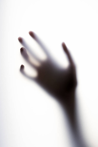Diffused shadow of hand with thin fingers behind the frosted glass - 写真・画像