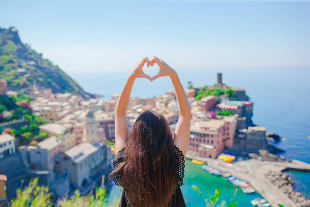 Beautiful girl making with hands heart shape on the old coastal town background of Vernazza, Cinque Terre National Park, Liguria, Italy ,Europe - Photo, Image