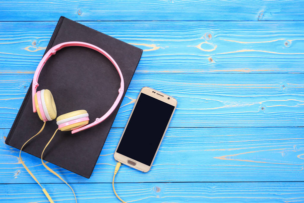 Smartphone, neuer moderner pinkfarbener Musikkopfhörer und Buch auf blauem Woo - Foto, Bild