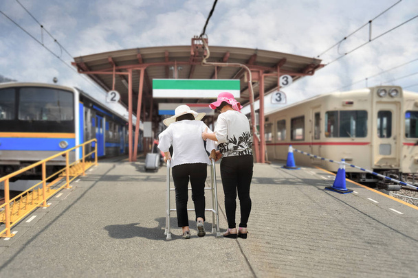 Filha cuidar mulher idosa andando na estação ferroviária, Japão
 - Foto, Imagem
