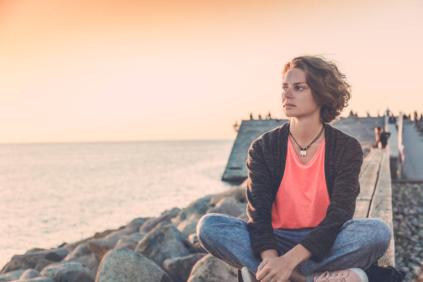 Beautiful young woman sitting on the beach watching the sunset - Zdjęcie, obraz