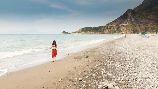 海岸で裸足で一人歩きの若い女性 - 写真・画像