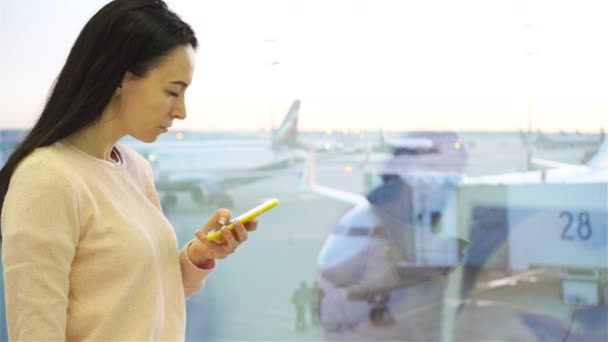 Portret młodej kobiety z smartphone w międzynarodowy port lotniczy. Pasażerów linii lotniczych w poczekalni czeka lot samolotu - Materiał filmowy, wideo