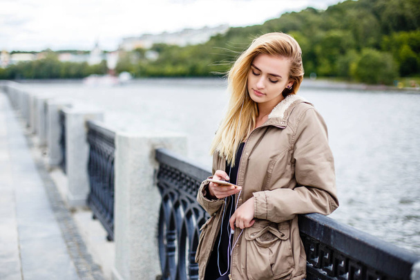 Attractive blonde girl walking along the promenade and listening to music with headphones - Fotografie, Obrázek