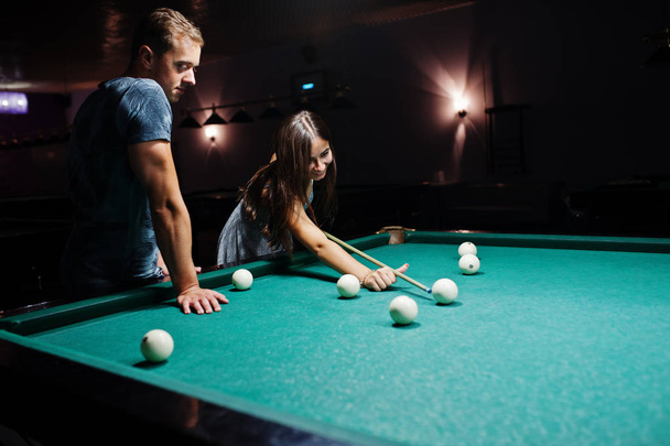Woman in dress playing pool with a man in a pub. - Photo, image