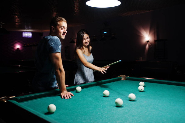 Woman in dress playing pool with a man in a pub. - Foto, afbeelding