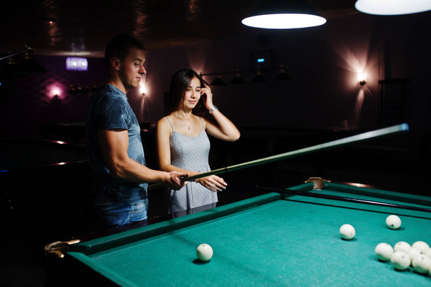 Woman in dress playing pool with a man in a pub. - Фото, зображення