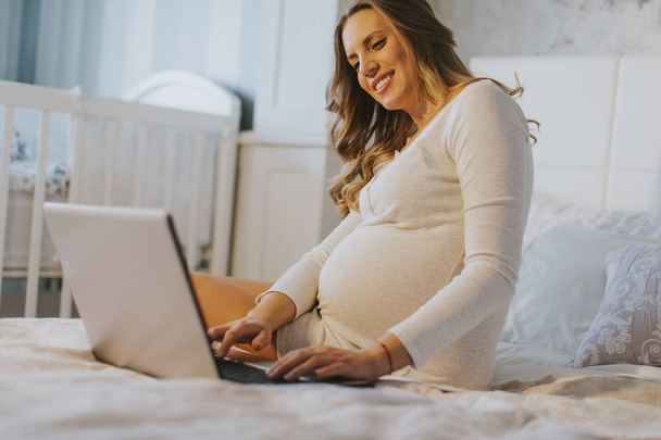 terhes nő az ágyban laptop - Fotó, kép