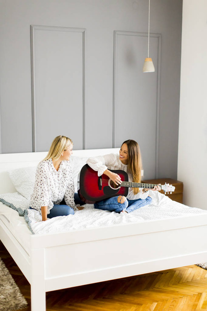 Two young women with guitar on bed - Фото, зображення