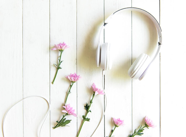 Top view headphones on white desk with pink flower and copyspace area for a text. Music and lifestyle Concept - Photo, image