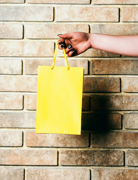 yellow shopping bag in female hand on brick wall - Foto, afbeelding