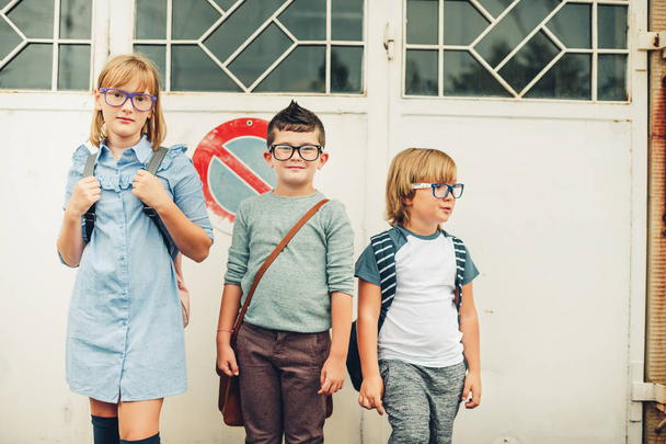 学校に歩いて戻ってのバックパックを身に着けている 3 人の面白い子供のグループ。女の子と男の子の屋外ポーズ眼鏡を着用 - 写真・画像