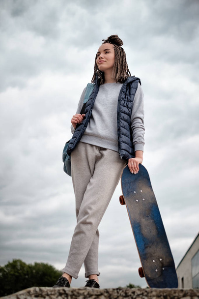 Hermosa chica hipster con tabla de skate de pie con sonrisa
 - Foto, Imagen