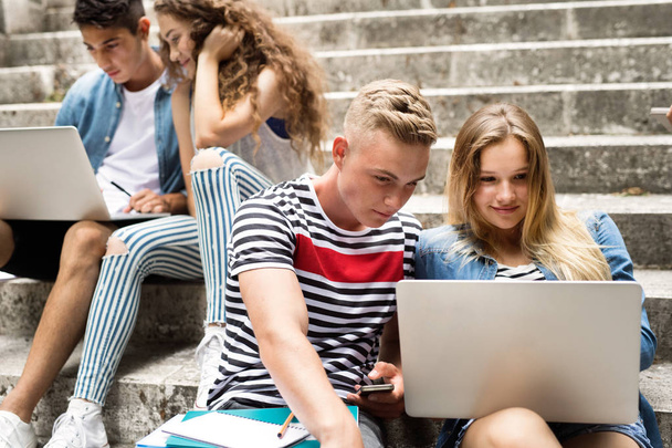 Teenage students with laptops sitting on stone steps. - Фото, изображение