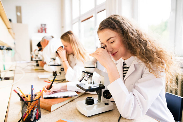 Beautiful high school students with microscopes in laboratory. - Foto, immagini