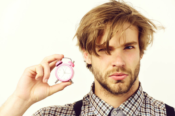 Man with serious face and beard holds pink alarm clock - Фото, изображение