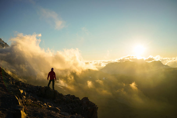 Una persona de pie en la montaña con nubes durante la puesta del sol / Sunr
 - Foto, Imagen