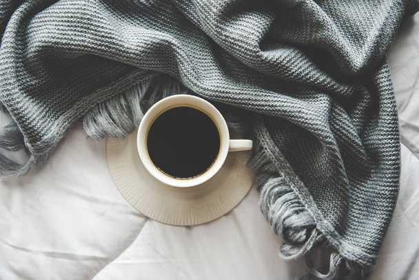 Cozy winter home background, cup of hot coffee with marshmallow, warm knitted sweater on white bed background, vintage tone.  Lifestyle concept - Photo, image