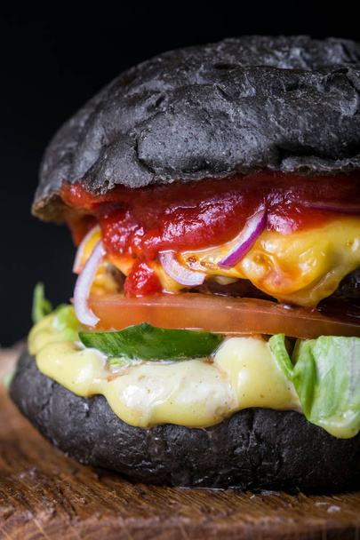 Fresh tasty burger on black background. Homemade hamburger with beef, onion, tomato, lettuce and cheese with ingredients - Photo, image