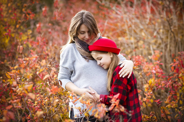 Happy young pregnant mother with daughter in autumn park - Photo, Image